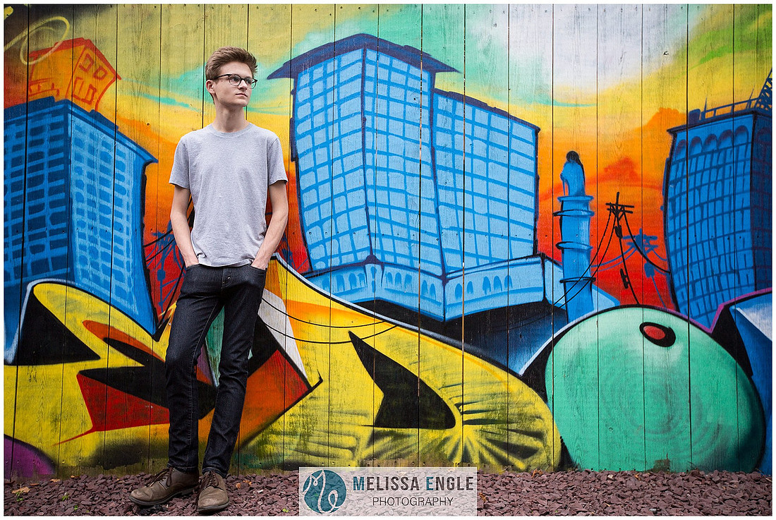 Creative senior portrait of a guy wearing glasses and skinny jeans against a colorful graffiti wall on West Grant Street in downtown Lancaster City.
