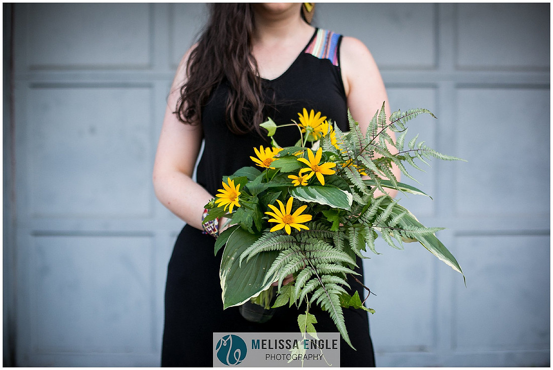 photo of a young woman in a black dress holding a wildflower bouquet of ferns, hostas and black eyed susans in Lancaster City, PA.