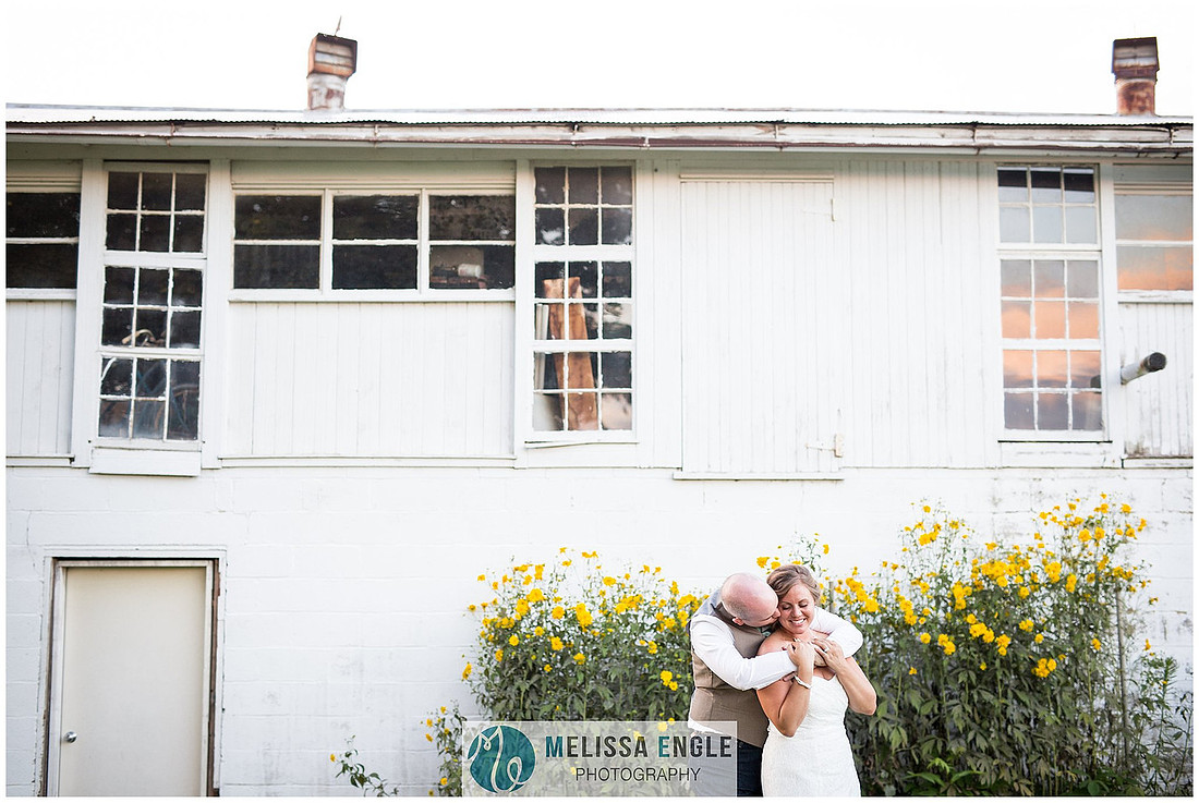 Beautiful photo of a bride and groom in front of a white barn with yellow flowers embracing one another at Springside Barn in Lancaster, PA.