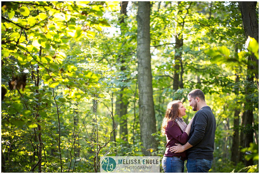 Engagement photo of a couple in the middle of the woods surrounded by trees, rocks and sunlight at Money Rocks County Park.