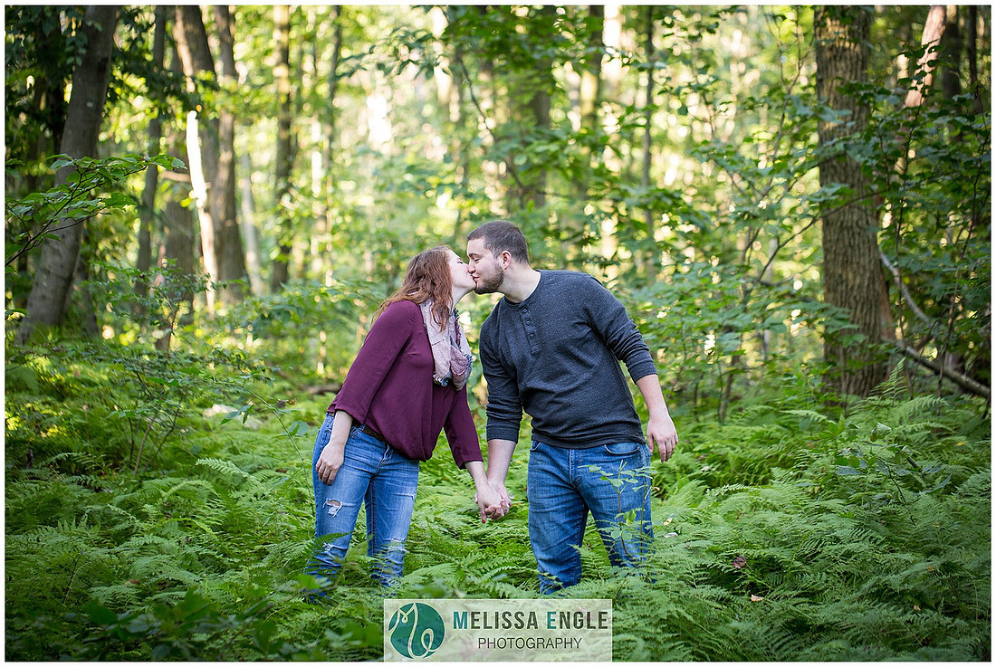Engagement photo of a couple in the middle of the woods surrounded by trees, rocks and sunlight at Money Rocks County Park.