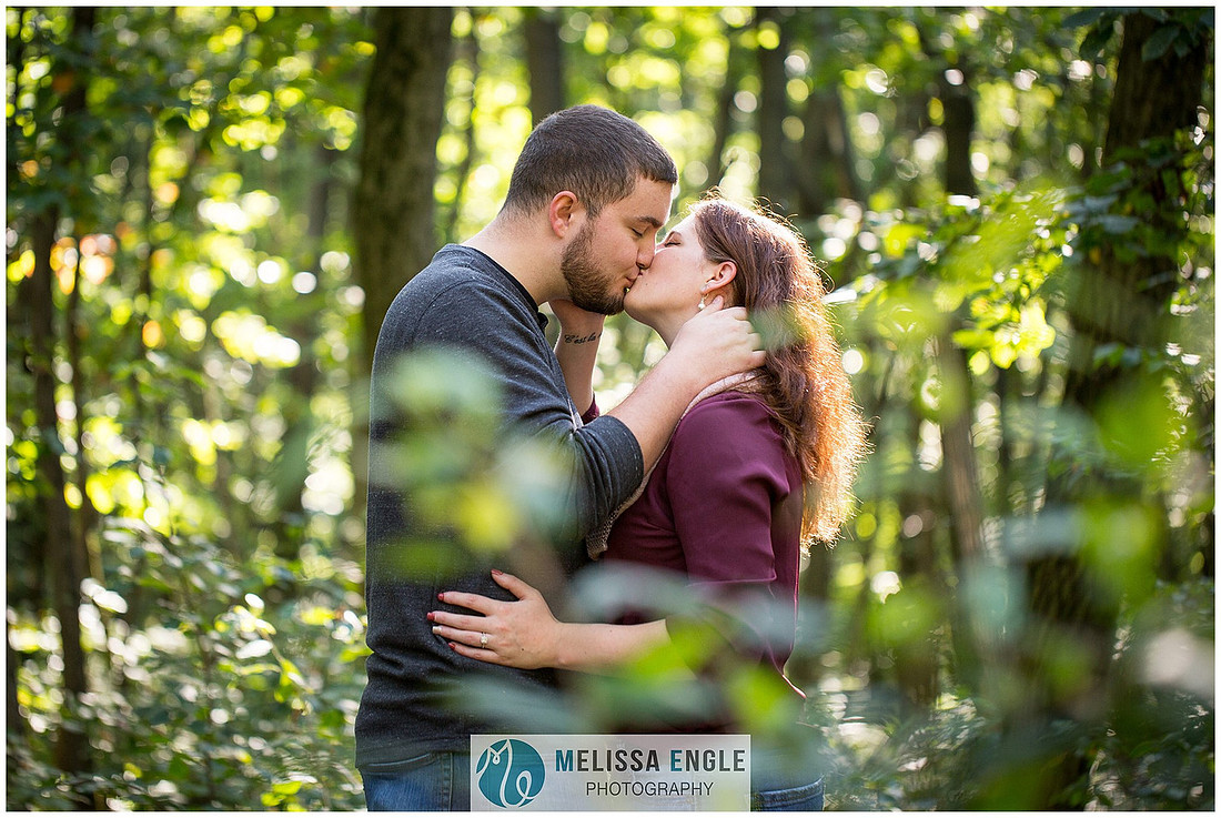 Engagement photo of a couple in the middle of the woods surrounded by trees, rocks and sunlight at Money Rocks County Park.