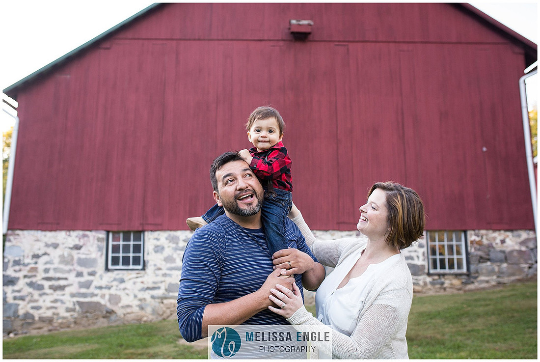 beautiful candid family photo of parents and a baby in front of a red barn in Lancaster, PA.