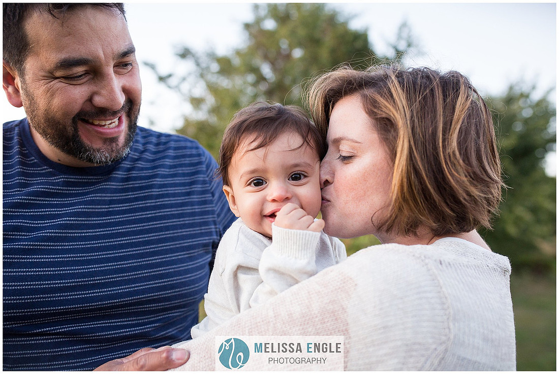 Sweet close up family portrait of a mother kissing her baby and an adoring father.