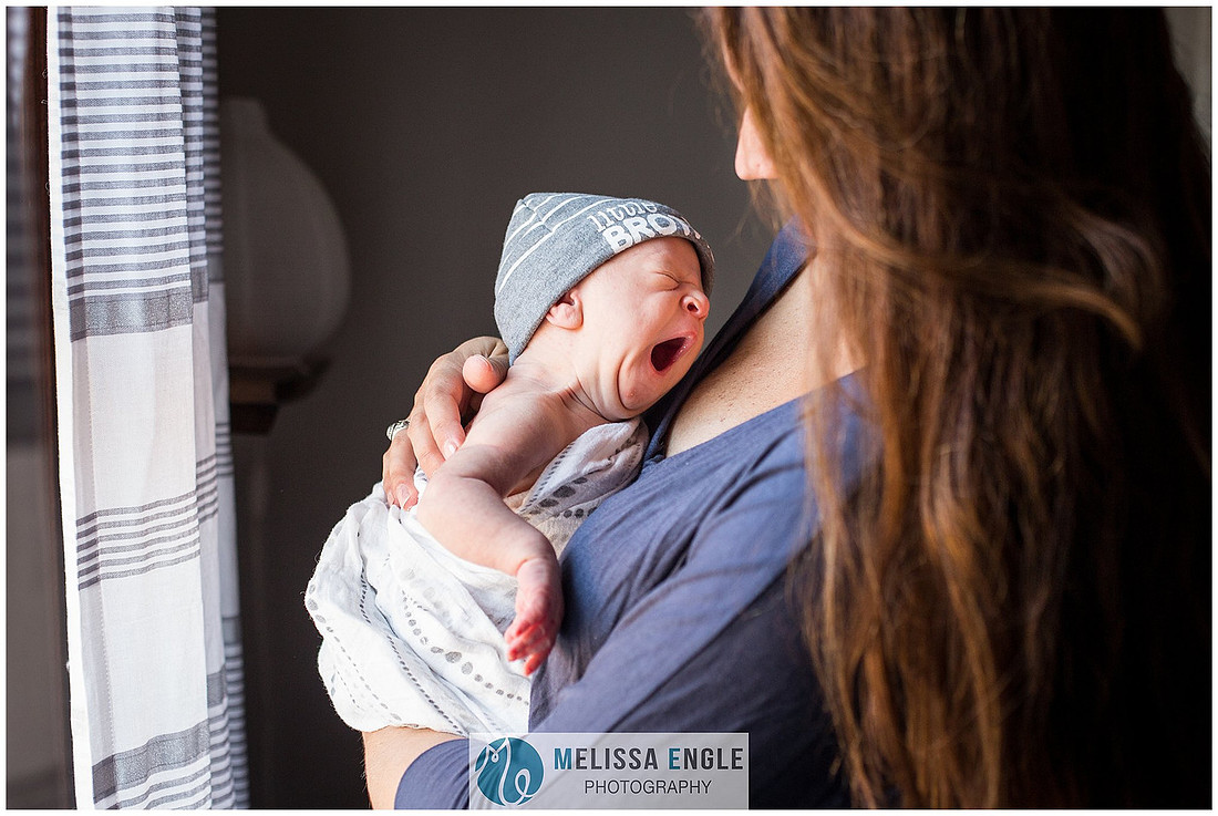 Photo of a young mother holding her newborn infant while he makes a big yawn.