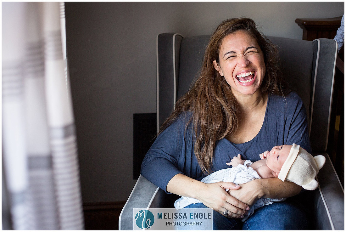 Photo of a young mother holding her newborn infant with a huge smile on her face.