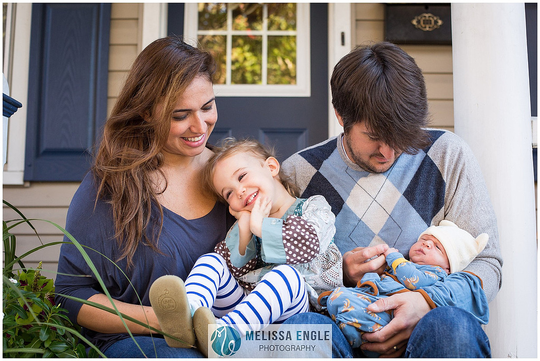 Photo of a young family of four, dad, mom, little girl and baby boy, smiling and laughing while sitting on their front porch in Lititz, Pennsylvania.