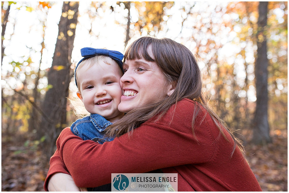 Photo of a mother hugging her daughter surrounded by bright autumn leaves in Lancaster, PA.