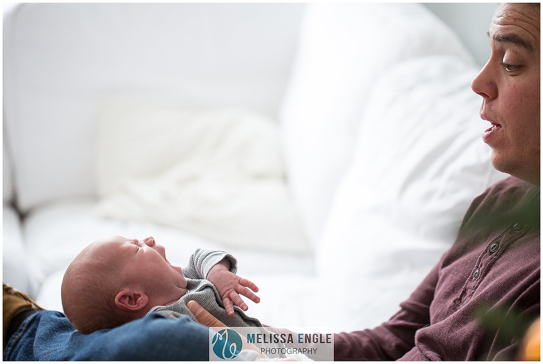 Photo of a father holding his newborn son while he is yawning.
